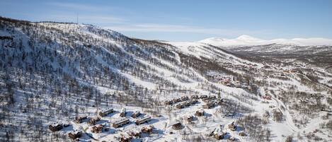 A snow-covered village with buildings arranged in a semi-circular pattern, surrounded by forested hills.