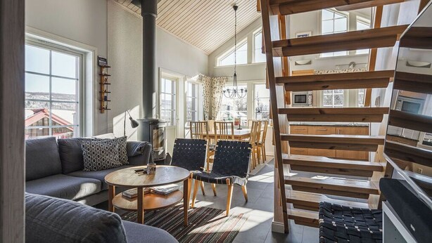 A modern interior with a sofa, chairs, a table, a staircase, and a kitchen area. - Blåstöten - Ramundberget (Bruksvallarna)