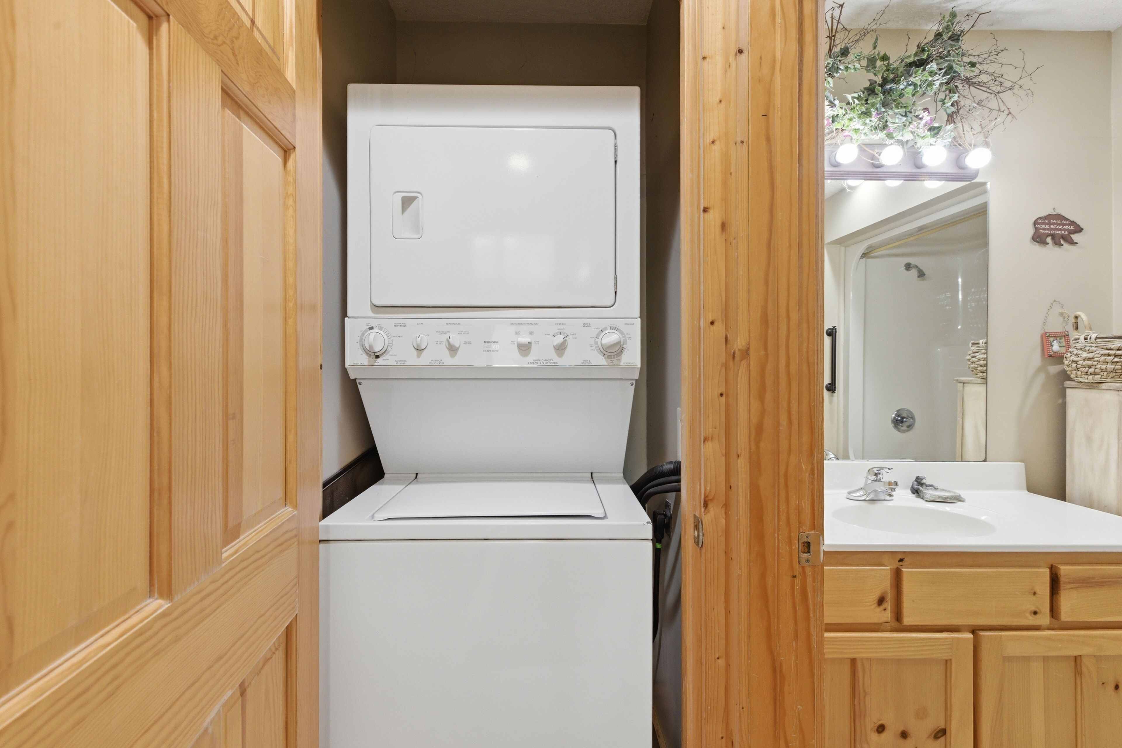 Une petite buanderie équipée d’un lave-linge et d’un sèche-linge, de meubles en bois, d’un évier et d’un miroir.