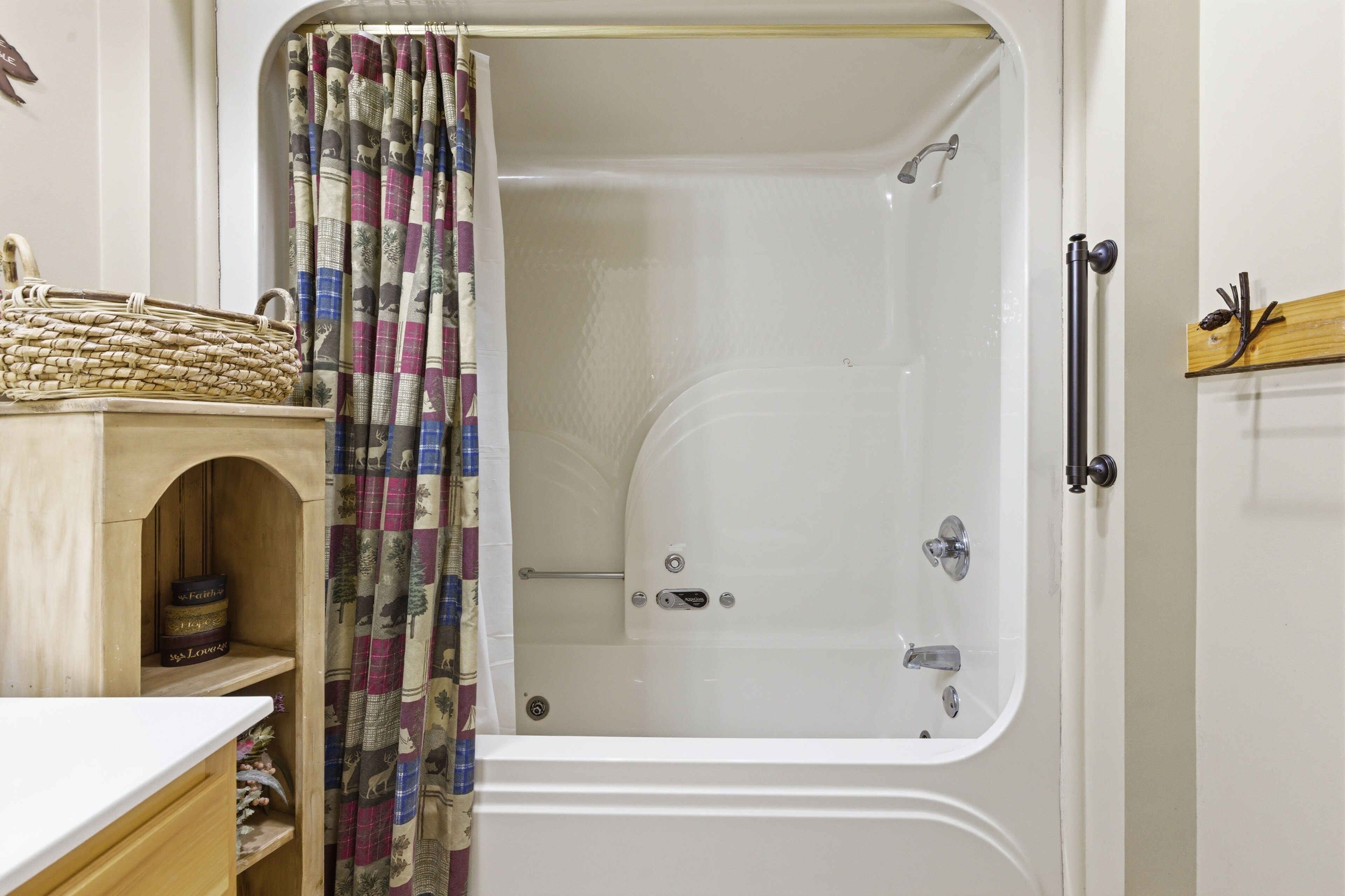 A bathroom with a shower, a wooden shelf with decorative items, and a patterned curtain.