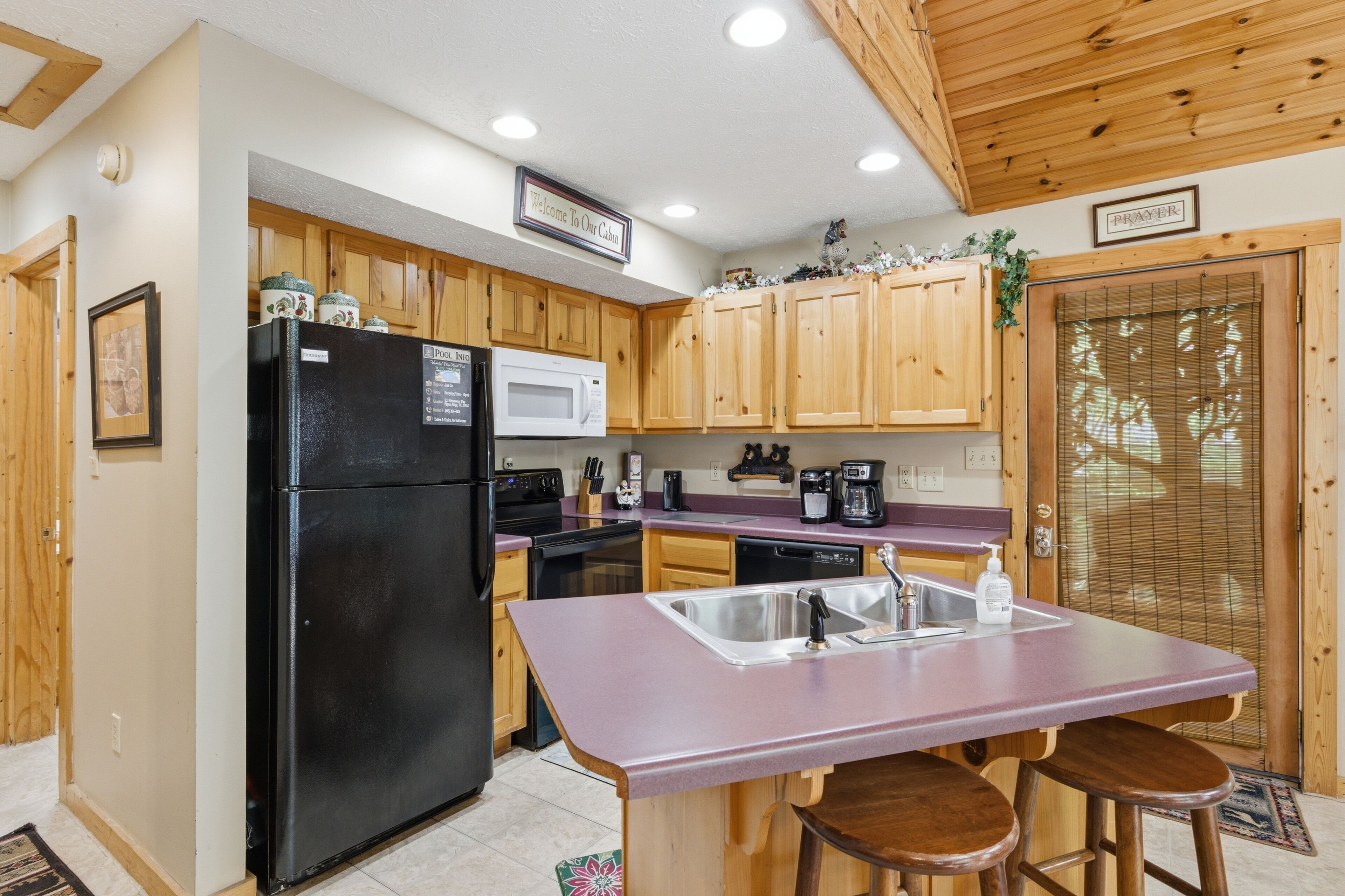 A kitchen with wooden cabinets, a black refrigerator, a microwave, a sink, and a bar stool.
