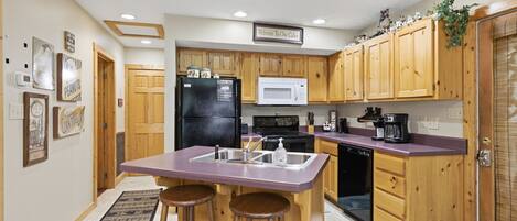A kitchen with wooden cabinets, a refrigerator, a microwave, a sink, and a bar stool.