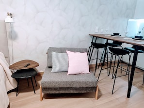 Un espace de vie moderne avec un canapé gris, une petite table ronde, un plancher en bois et un coin repas comprenant des chaises et une table.