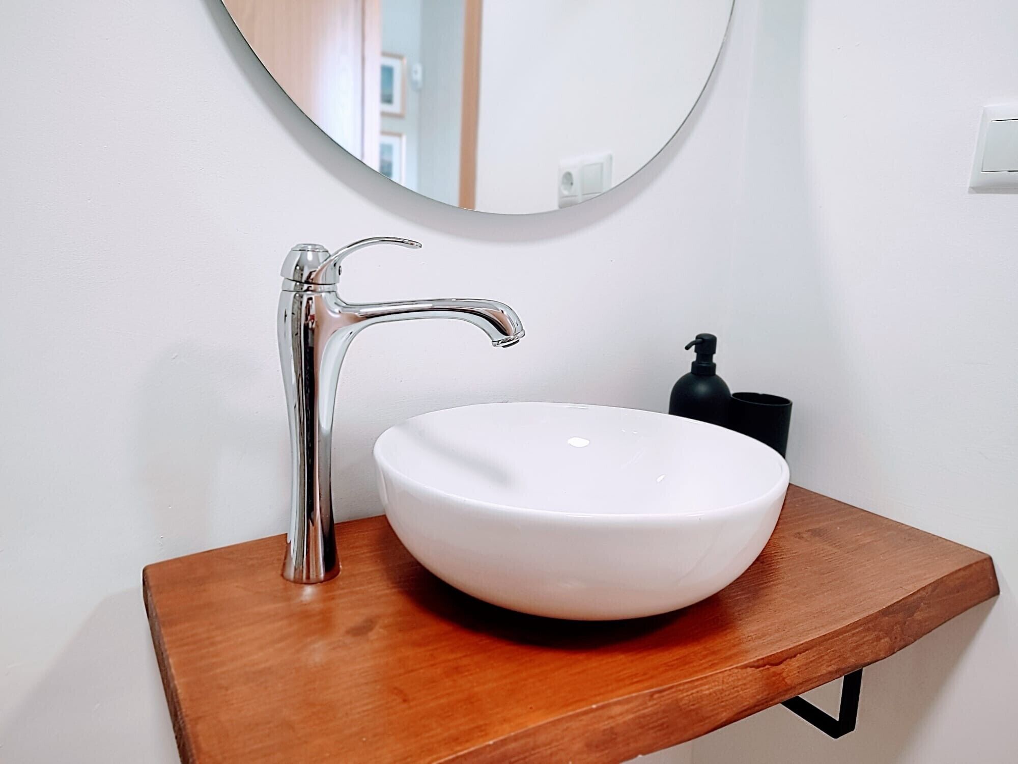 A bathroom with a white sink, chrome faucet, and a round mirror.