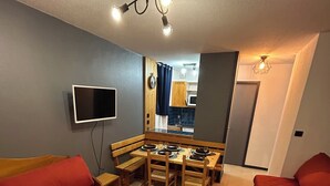 Ein kompakter Wohnraum mit Sofa, Couchtisch, Fernseher, Esstisch und Küchenzeile.