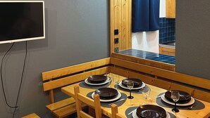 Ein Essbereich mit einem Holztisch, gedeckt für vier Personen, einem an der Wand befestigten Fernseher und einem Holzschrank im Hintergrund.