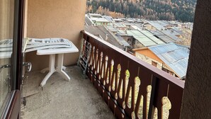 Ein Balkon mit Tisch und Stühlen, Blick auf einen bewaldeten Hang und eine Wohngegend darunter.