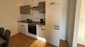 Eine kleine Küche mit Herd, Backofen und Spüle. Es gibt einen Essbereich mit Stühlen und einem Tisch.