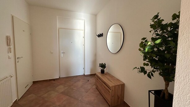 Ein Flur mit einer Holzbank, einem Blumentopf, einem runden Spiegel und einer Tür.