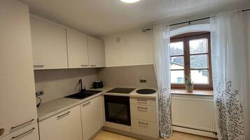 A compact kitchen with white cabinets, a stove, a sink, and a window with a view of trees.