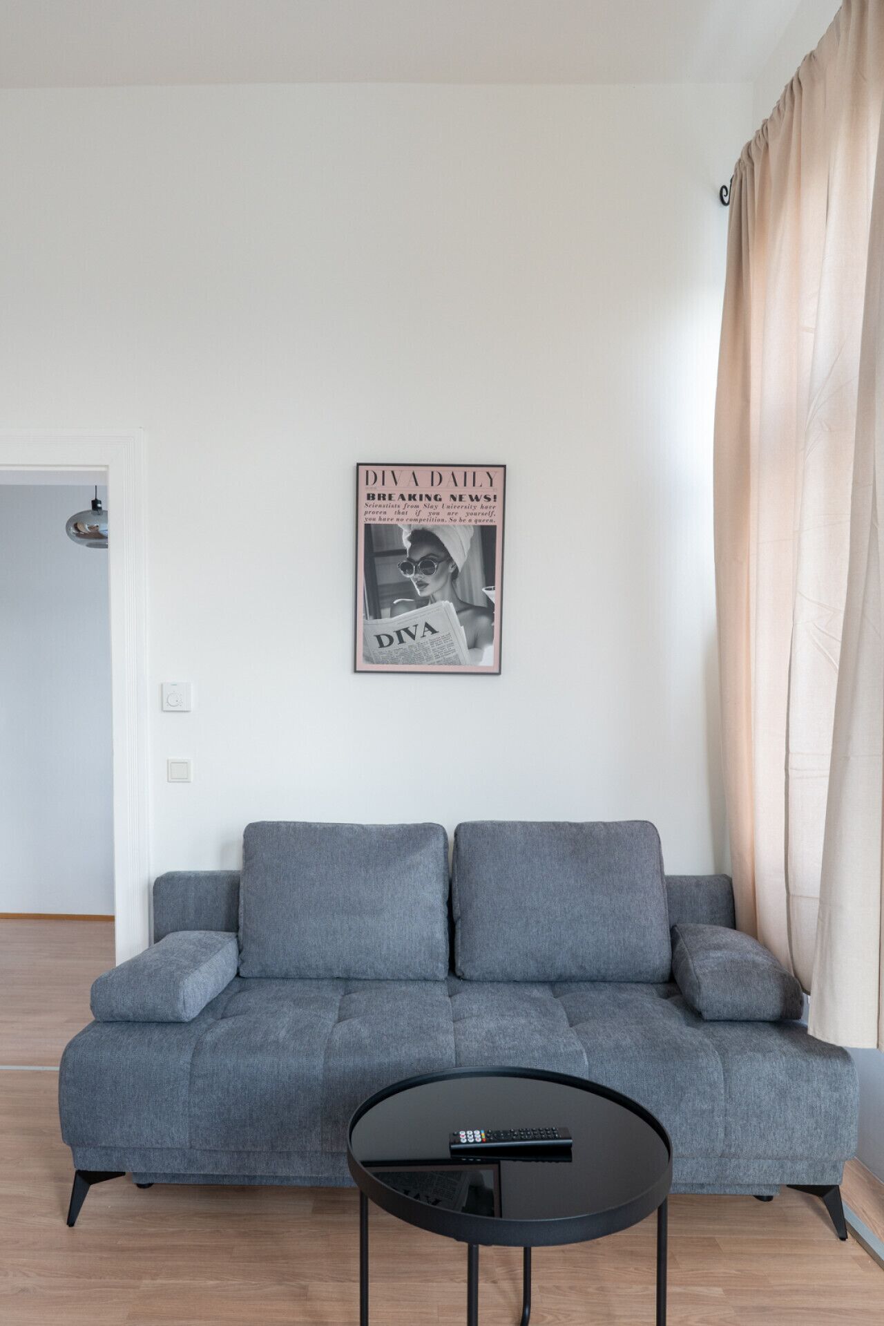 Una sala de estar con un sofá gris, una mesa de centro negra y un cuadro en la pared.