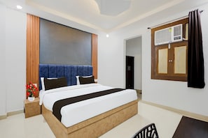 Een moderne hotelkamer met een groot bed, een houten hoofdeinde, een nachtkastje met een bloemenvaas en een raam met gordijnen.