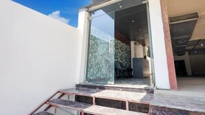 Ingresso moderno di un edificio con porta in vetro, una scala che sale e un interno visibile con parete decorata e una scrivania.