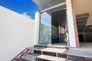 A modern building entrance with a glass door, a staircase leading up, and a visible interior with a patterned wall and a desk.