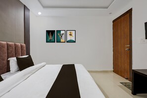 A hotel room with a bed, a wooden door, and three framed artworks on the wall.