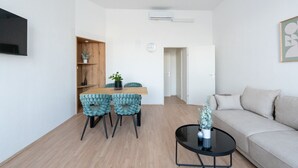 Un salon moderne avec une table à manger en bois, des chaises recouvertes d’un tissu turquoise, une table basse ronde noire et un canapé beige.