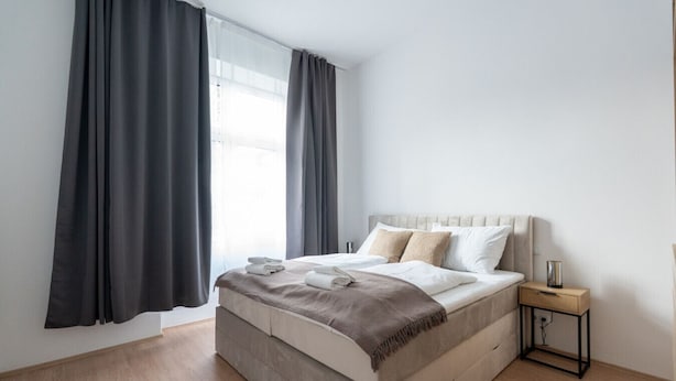 Une chambre d’hôtel moderne avec un grand lit, une table de chevet et une fenêtre avec des rideaux.