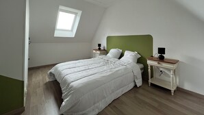Ein Schlafzimmer mit schrägem Dach, einem Oberlicht, einem Bett mit weißer Bettwäsche, zwei Nachttischen mit Lampen und einem Holzboden.