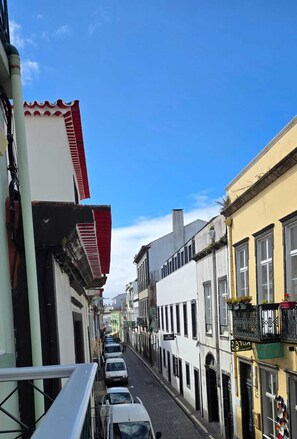 A narrow street with buildings on either side, a clear blue sky, and parked cars. - AP200 (Ponta Delgada)