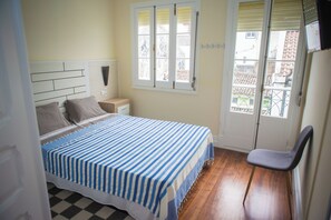 A bedroom with a bed, a nightstand, a chair, a window, and a door. - AP200 (Ponta Delgada)