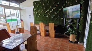 Una stanza con un tavolo e sedie in legno, una televisione fissata a una parete verde e una pianta in vaso.