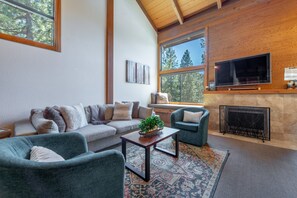 Ein Wohnzimmer mit einer Couch, Sesseln, einem Couchtisch, einem Kamin und einem an der Wand befestigten Fernseher.