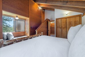 Ein Schlafzimmer mit einem großen Bett, Holzwänden, einem Fenster mit Aussicht und einer Treppe.
