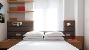 Een moderne slaapkamer met een bed, twee nachtkastjes, een houten hoofdbord, een plank met boeken en een raam met dunne gordijnen.