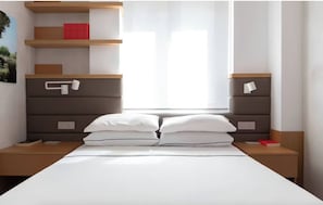 A modern bedroom with a bed, two nightstands, a wooden headboard, a shelf with books, and a window with sheer curtains. - Luxury designer apartment in the heart of Rome (Roma)