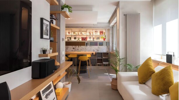 Een moderne woonkamer met een bank, een televisie en een keukenhoek met een eettafel en stoelen.