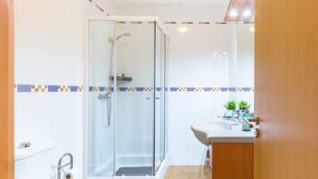 A bathroom with a glass-enclosed shower, a toilet, and a sink with a mirror.