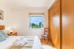 Ein Schlafzimmer mit Bett, Fenster, Sessel, Nachttisch und Kleiderschrank.