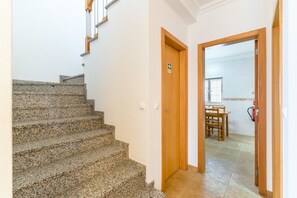 Eine Treppe führt zu einem Raum mit einer Holztür, einem Essbereich mit Tisch und Stühlen sowie einer durch eine offene Tür sichtbaren Küche.