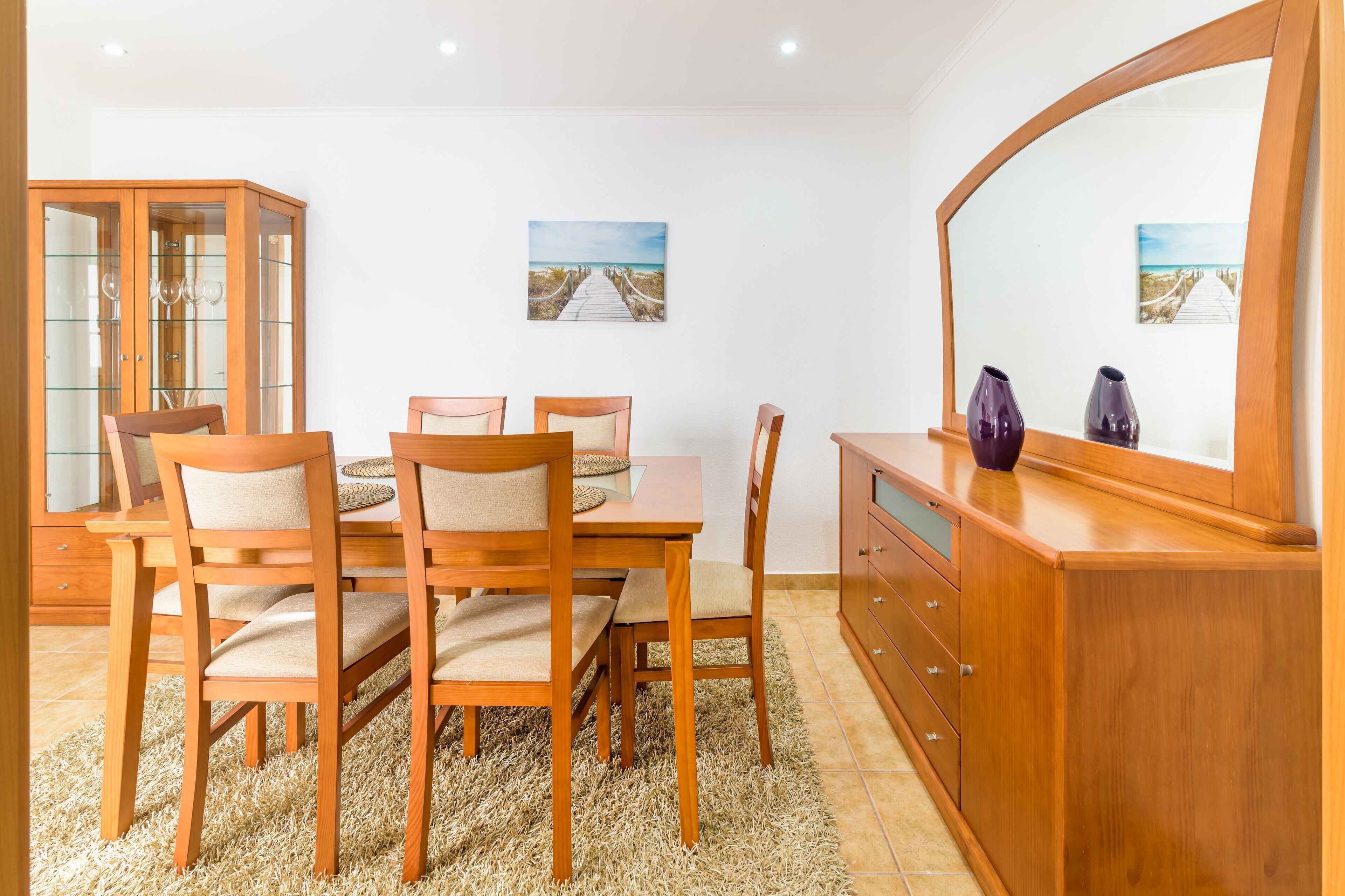 A dining area with a wooden table and chairs, a cabinet, and two framed pictures on the wall.