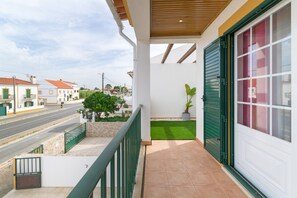 A balcony with a view of a street, a green railing, a potted plant, and a door with green shutters. - Malibu Guest House Holiday Home with Private Terrace, Wi-Fi, and Air Conditioning (Vila Nova de Milfontes)