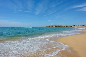 A beach with clear blue water, a sandy shore, and a distant building on a hill.