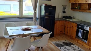 Uma cozinha compacta com armários de madeira, geladeira, mesa de jantar com cadeiras e uma janela com cortinas.
