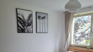 Quarto com cama de madeira, tapete xadrez preto e branco, duas imagens emolduradas na parede e uma janela com cortinas.
