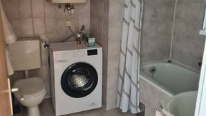 Uma casa de banho compacta com máquina de lavar roupa, sanita e banheira.