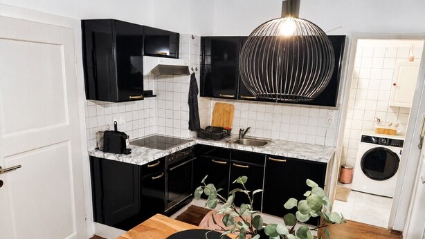 A modern kitchen with black cabinets, a marble countertop, and a wooden dining table with black placemats. - Faraway Homes Studio Enns #14 (Enns)