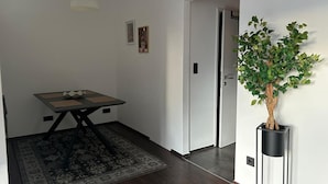 Une pièce comprenant une table à manger, un tapis, une plante en pot et une porte donnant sur une autre pièce.