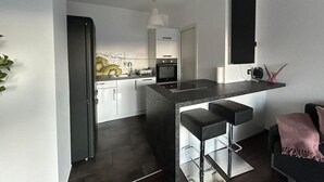 Une cuisine moderne dotée d’un îlot central, de tabourets de bar et d’un coin repas avec un canapé noir et un plaid rose.