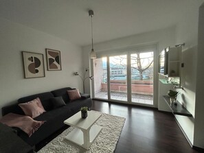 A modern living room with a black sofa, a white coffee table, and a large window with a view of the city.