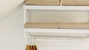 Een witte muur met een wit wandrek met daarin twee beige kussens en een houten hanger.