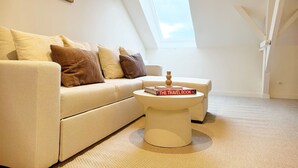 Een knus loft slaapkamer met een hoge en schuine plafond, een dakraam, een witte bank, een witte salontafel en een klein nachtkastje.
