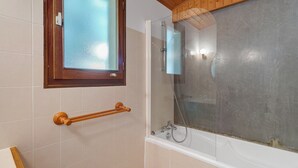 Une salle de bain avec une douche à parois de verre, une fenêtre en bois et une baignoire blanche.