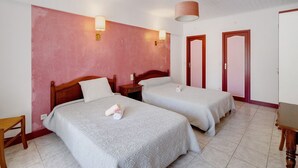 Une chambre d’hôtel avec deux lits, une table de chevet en bois, une chaise en bois et une porte rouge.