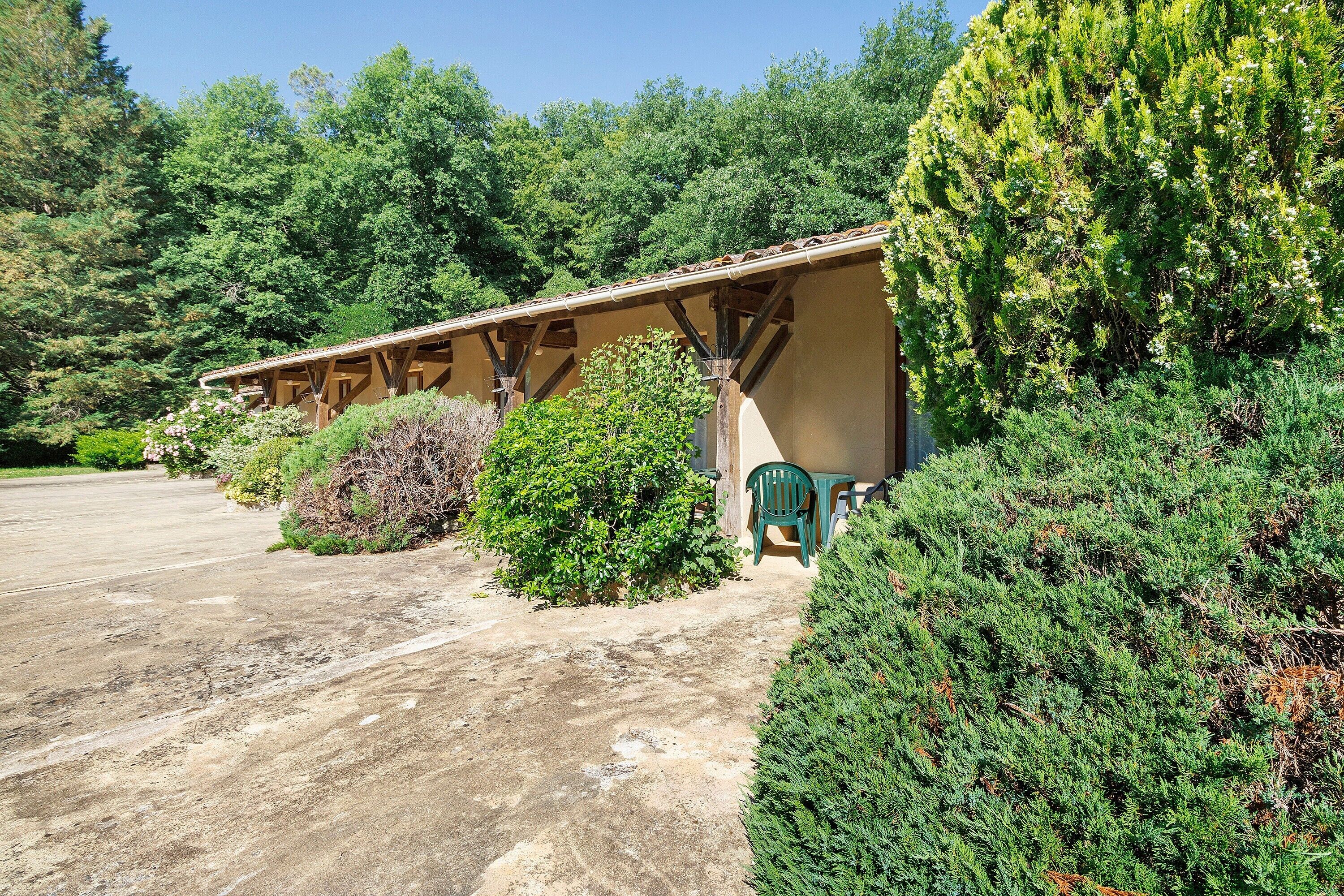 Un bâtiment de style rustique doté d’un porche couvert, entouré d’une végétation luxuriante et bordé d’une allée pavée.