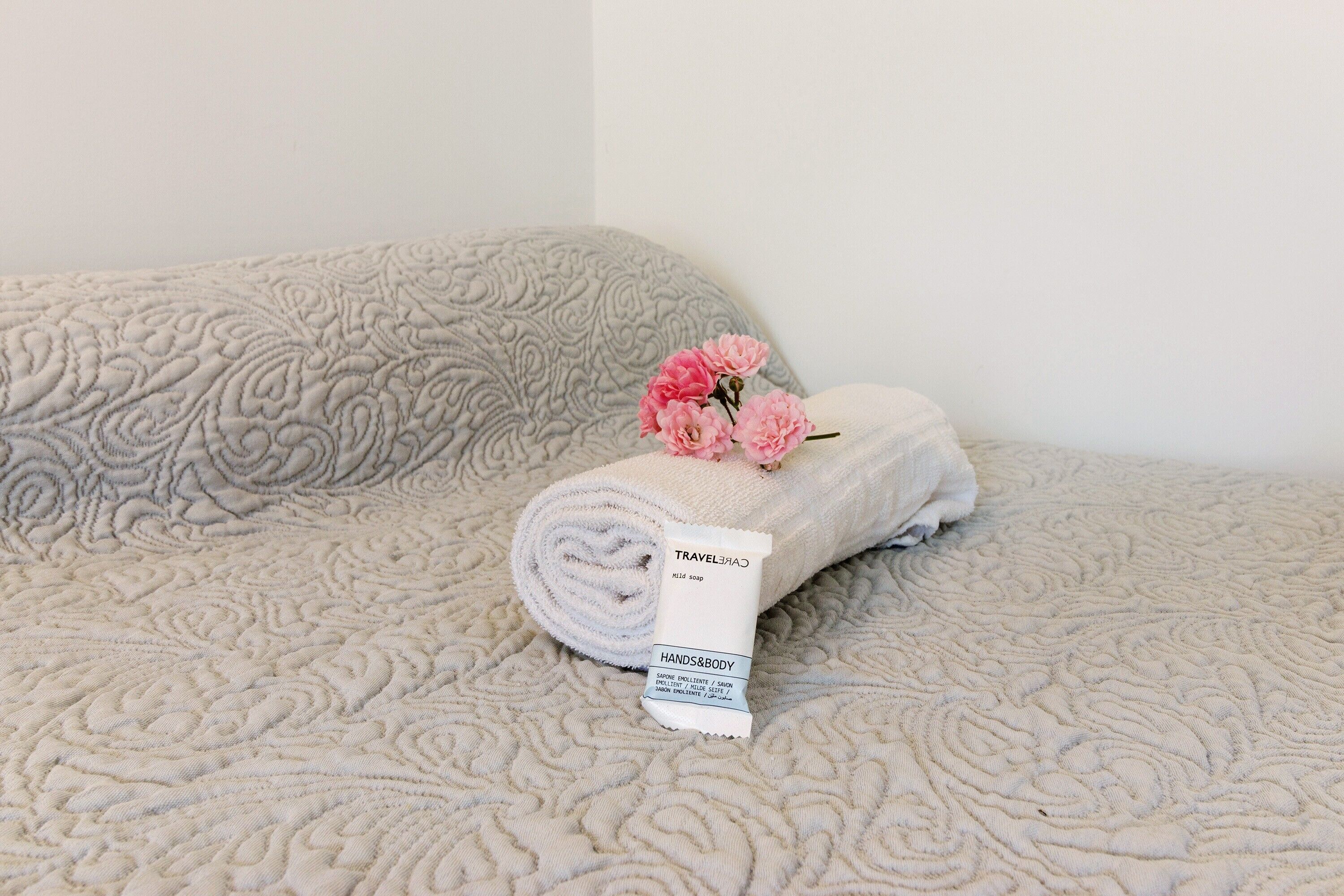 A bed with a rolled towel and a travel-sized hands and body soap.