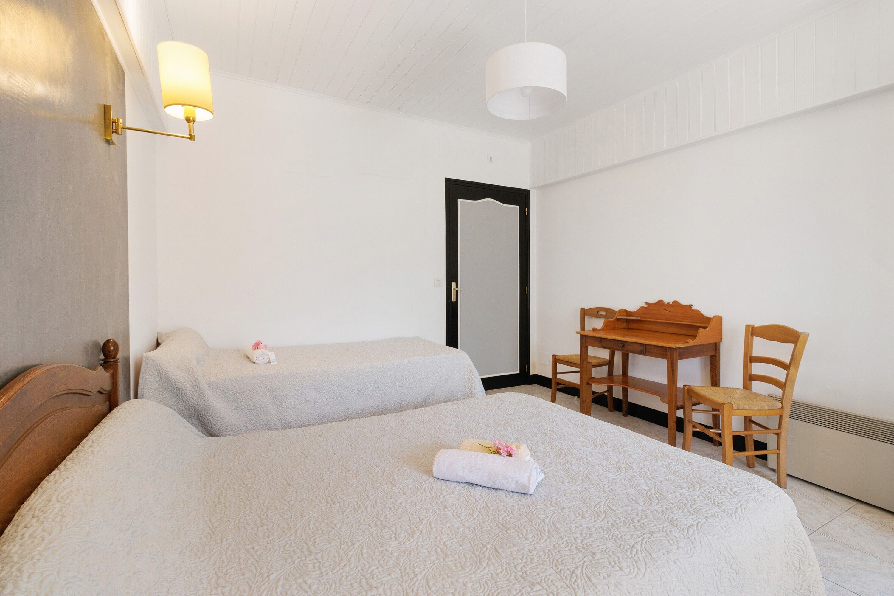 A hotel room with two beds, a wooden desk, a chair, and a mirror.